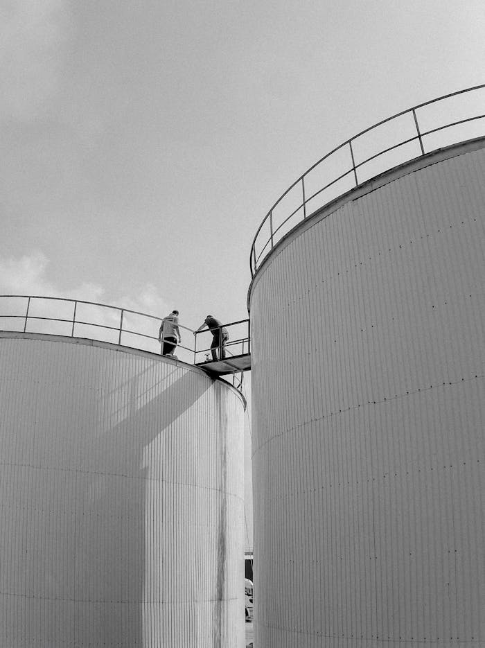 Men atop industrial silos in Adana, Türkiye. Monochrome image.